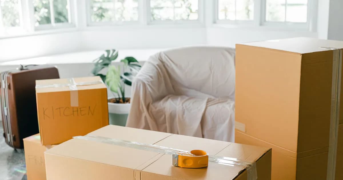 Various cardboard boxes with household belongings and suitcase placed on floor