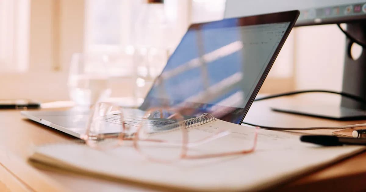 A well-lit home office setup featuring a laptop, monitor, and glasses