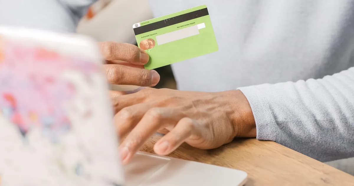 Close-up of hands holding a green credit card for an online purchase using a laptop