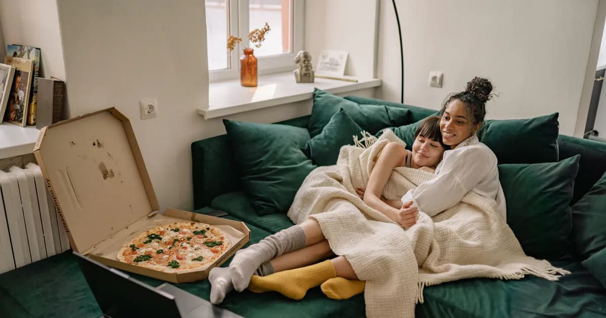 Lesbian couple cuddles on the couch while enjoying a pizza and relaxation at home
