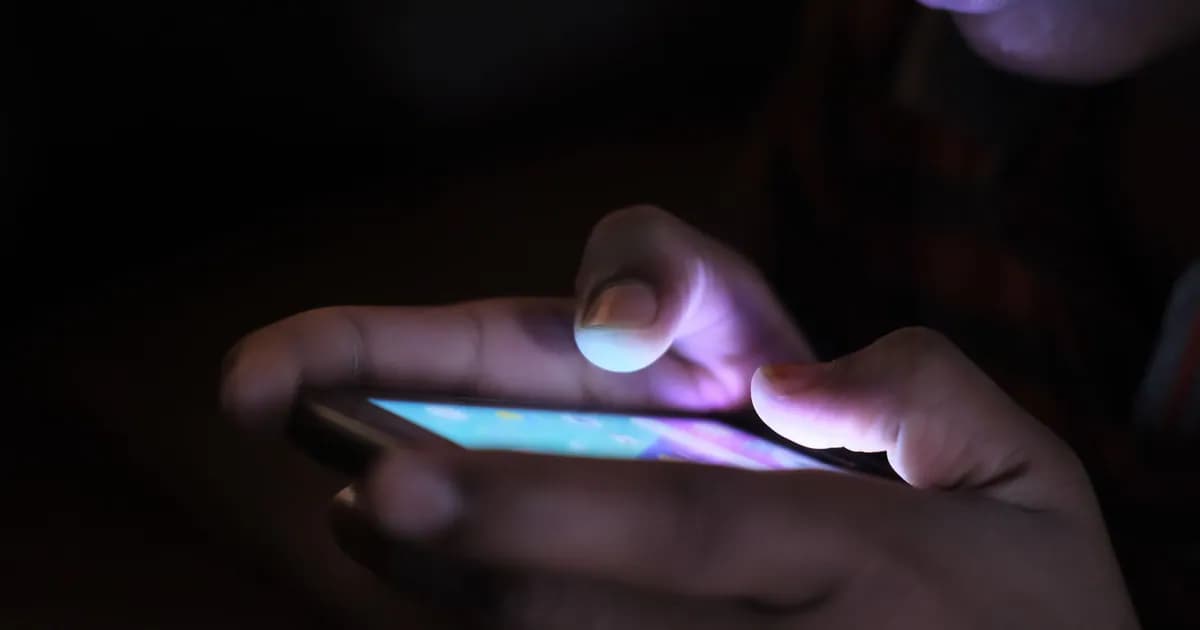 Close-up of a person holding and using an illuminated smartphone in a dark setting