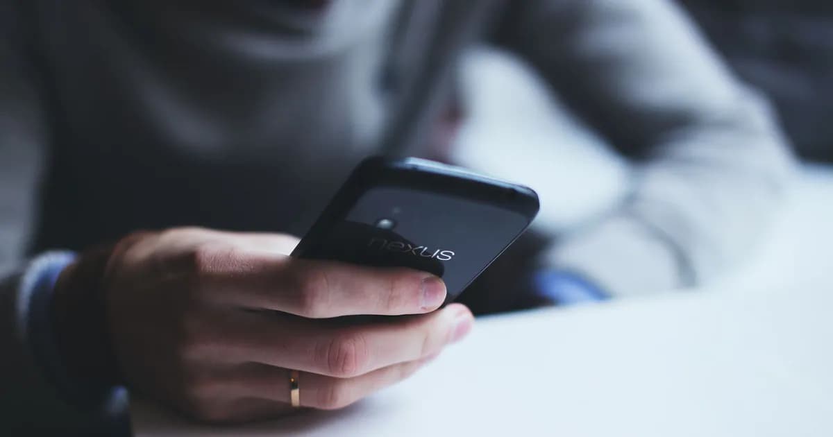 Close-up of a person holding a smartphone while sitting at a white table
