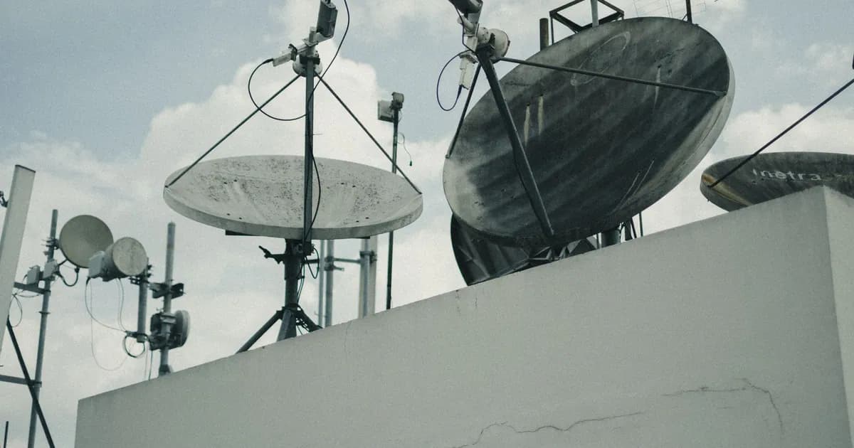 A detailed view of satellite dishes and antennas on an urban rooftop under a cloudy sky