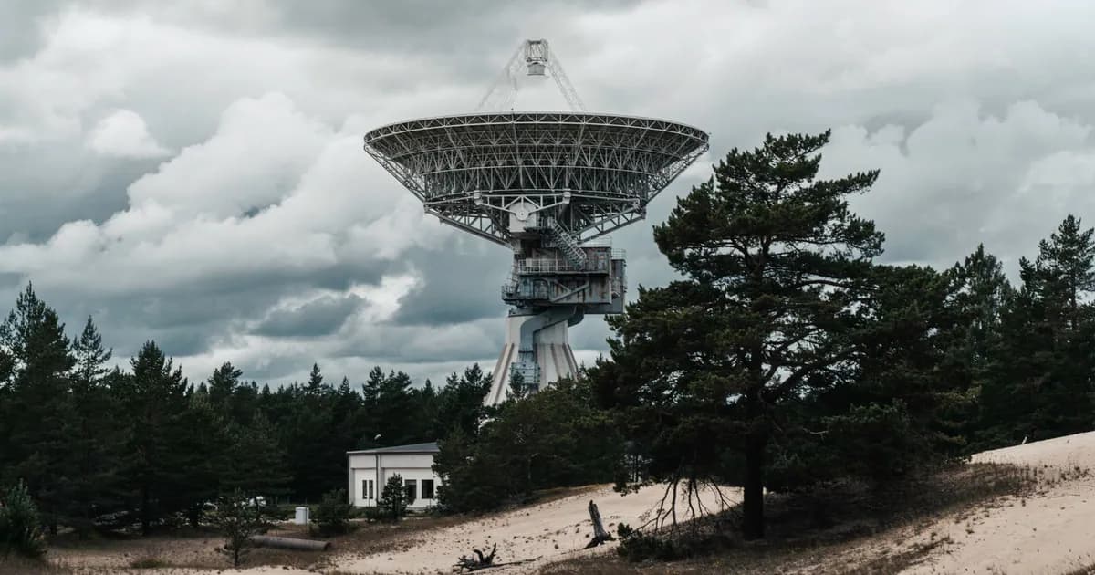 A large radio telescope tower stands in a forest under dramatic clouds
