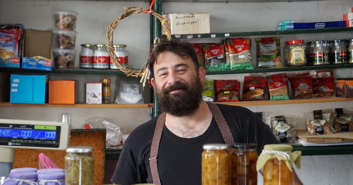 A friendly shopkeeper stands behind shelves of homemade preserves