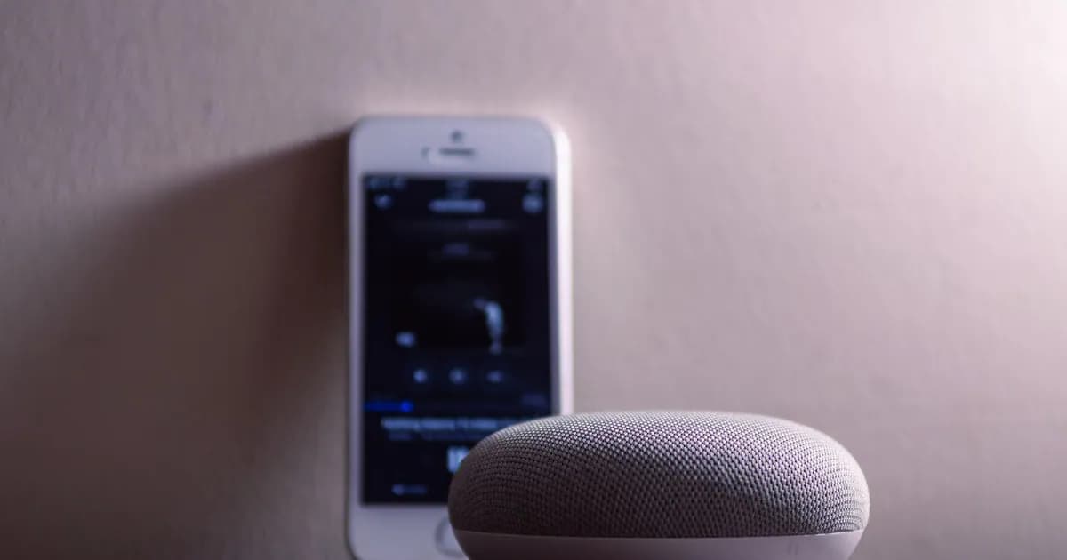 A modern smart speaker and smartphone on a wooden table, indoors