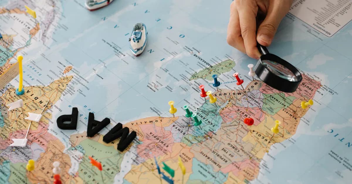 A hand using a magnifying glass over a world map with pins and toy ships