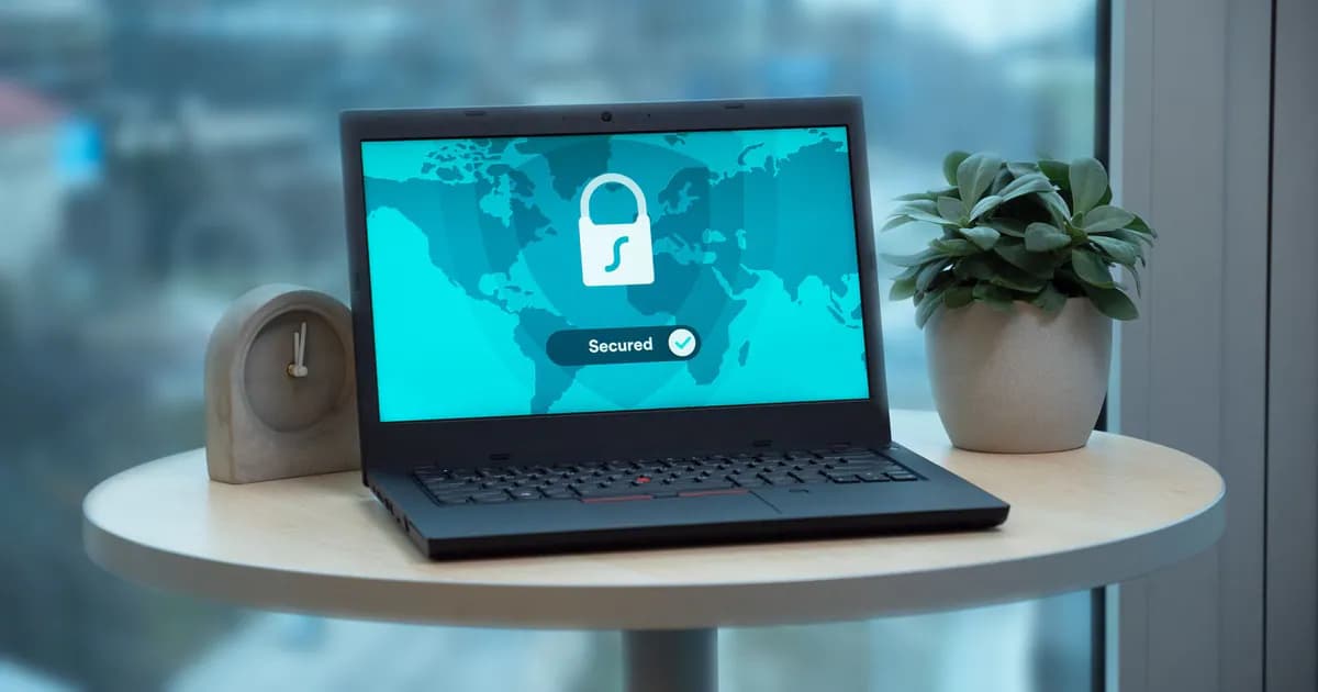 Laptop displaying a security lock icon on a table with a potted plant and clock