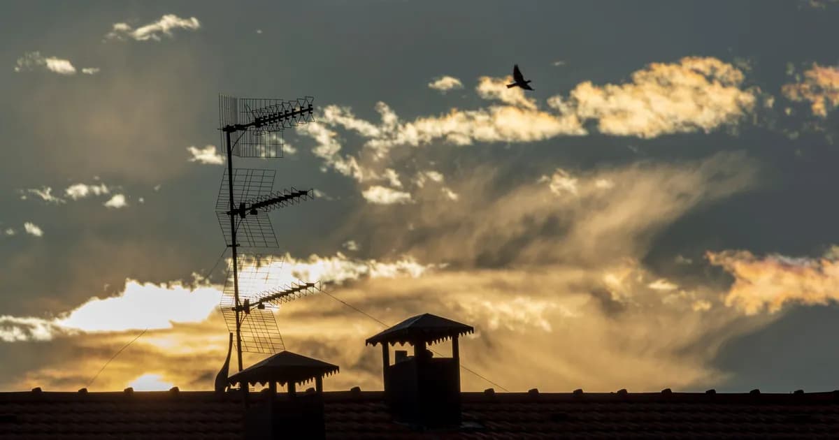 A captivating rooftop silhouette with antenna and bird against a dramatic sunset sky