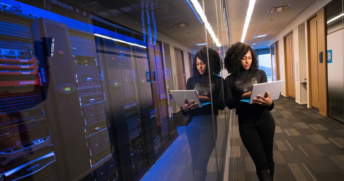 A woman using a laptop navigating a contemporary data center with mirrored servers
