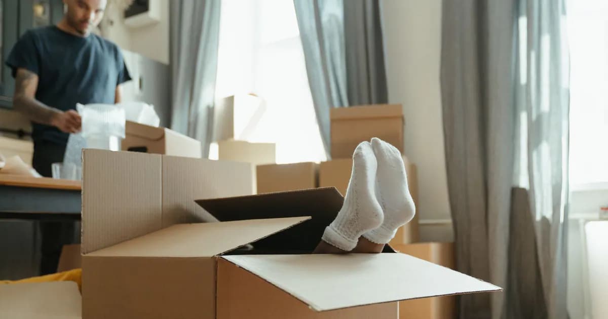 A playful scene of feet sticking out of a cardboard box during moving day in a bright, indoor setting