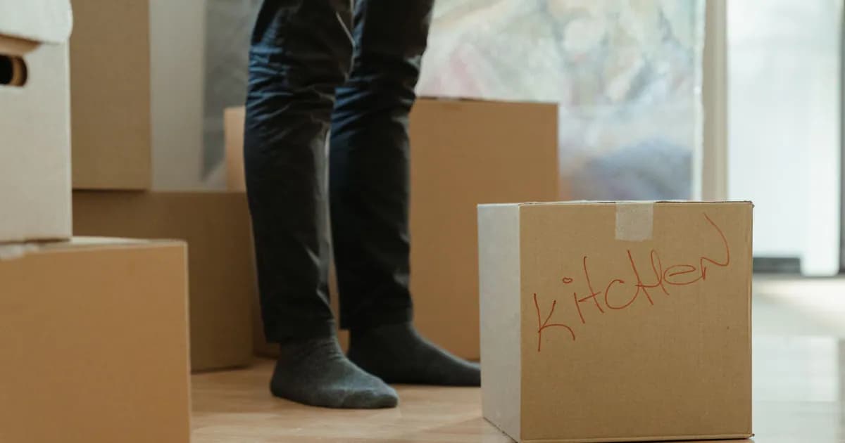 A person standing in a room surrounded by moving boxes labeled for the kitchen
