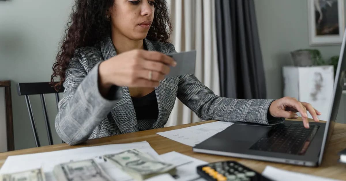 Woman using a laptop and managing finances with cash and card on a wooden table indoors
