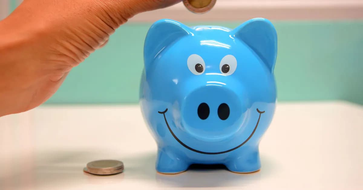 Hand inserting a coin into a blue piggy bank for savings and money management