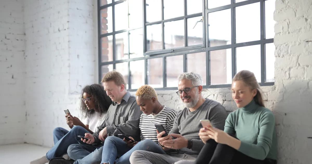 Smiling coworkers of different ages in casual outfit browsing internet on cellphones while sitting