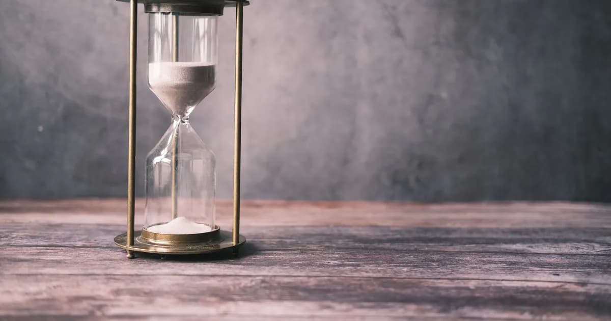 A classic hourglass with sand on a rustic wooden table against a soft gray background, offering ample copy space