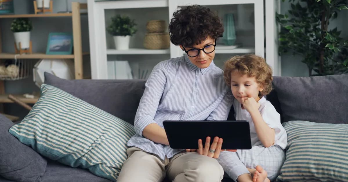 A parent and child sit on a couch engaging with a tablet indoors