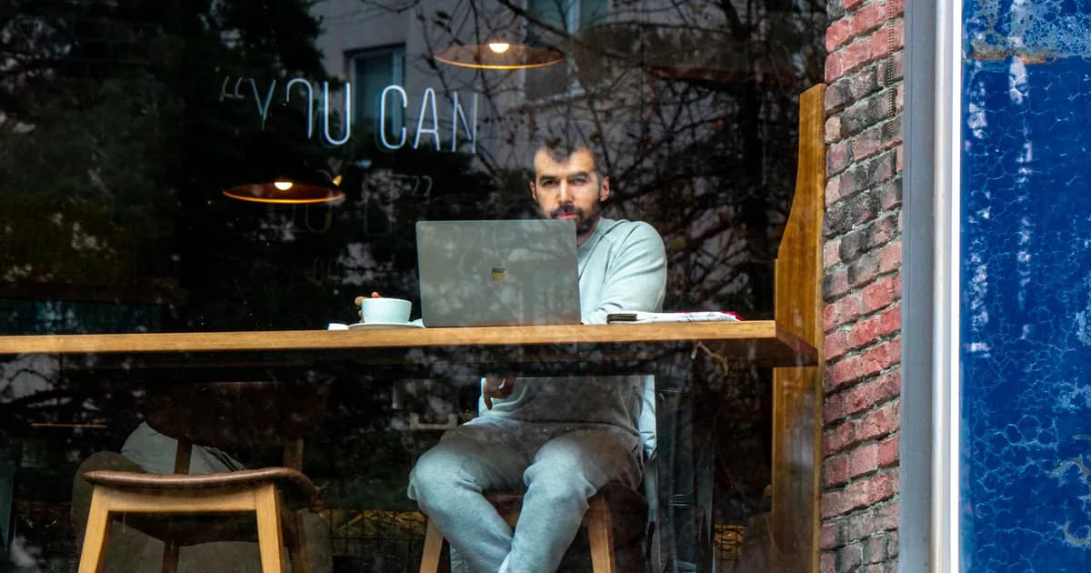 Young man working on laptop in a café, seen through window. Cozy indoor setting