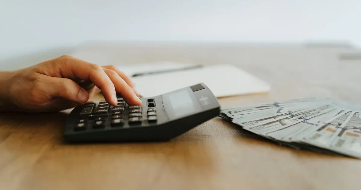 A hand calculating finances with a calculator next to stacks of US dollar bills