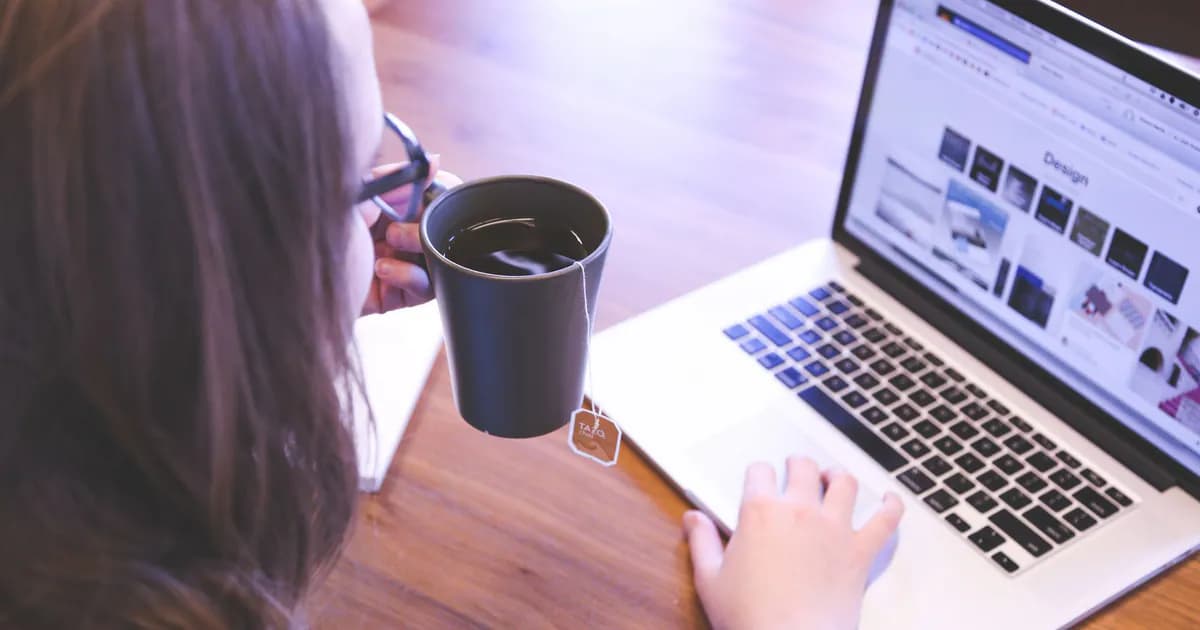 A woman enjoys coffee while browsing the web on a laptop at a home office desk