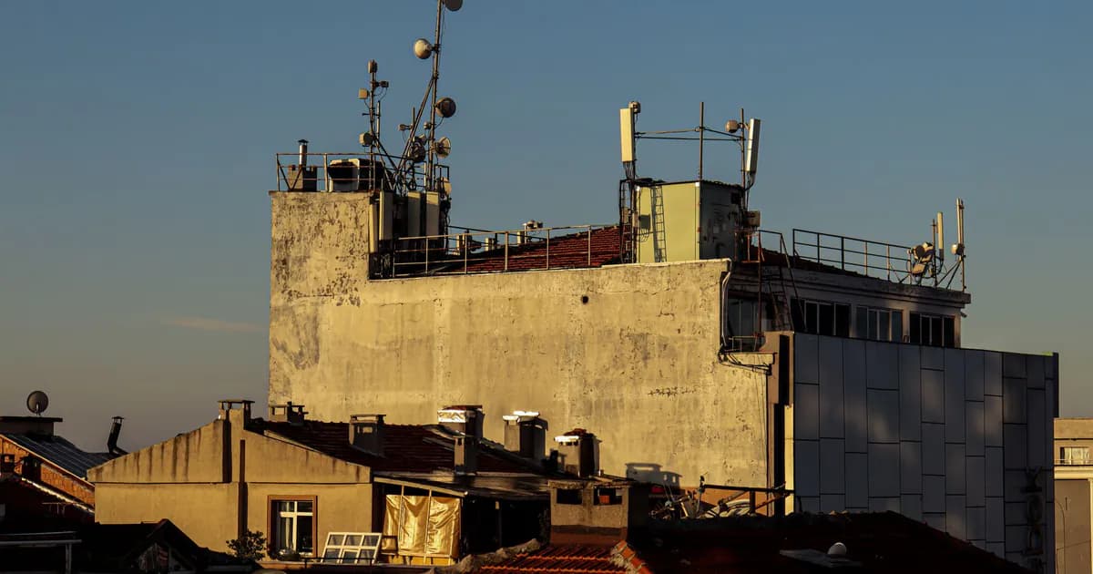 A city rooftop with antennas and relay towers against a clear blue sky at sunset