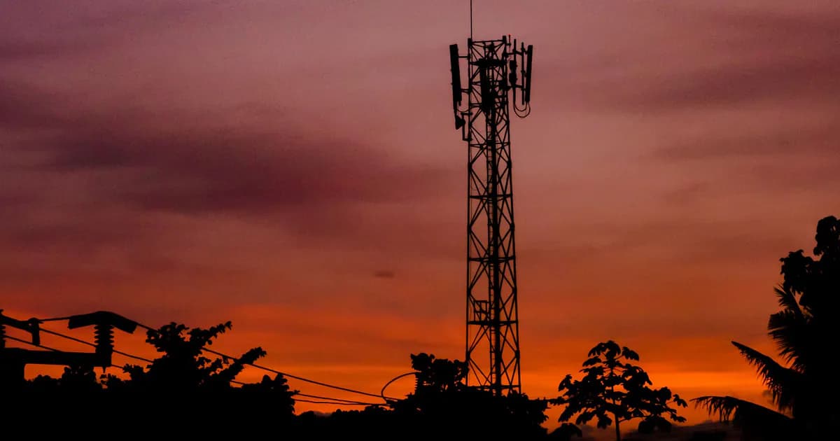 A silhouette of a telecommunication tower against a dramatic sunset sky