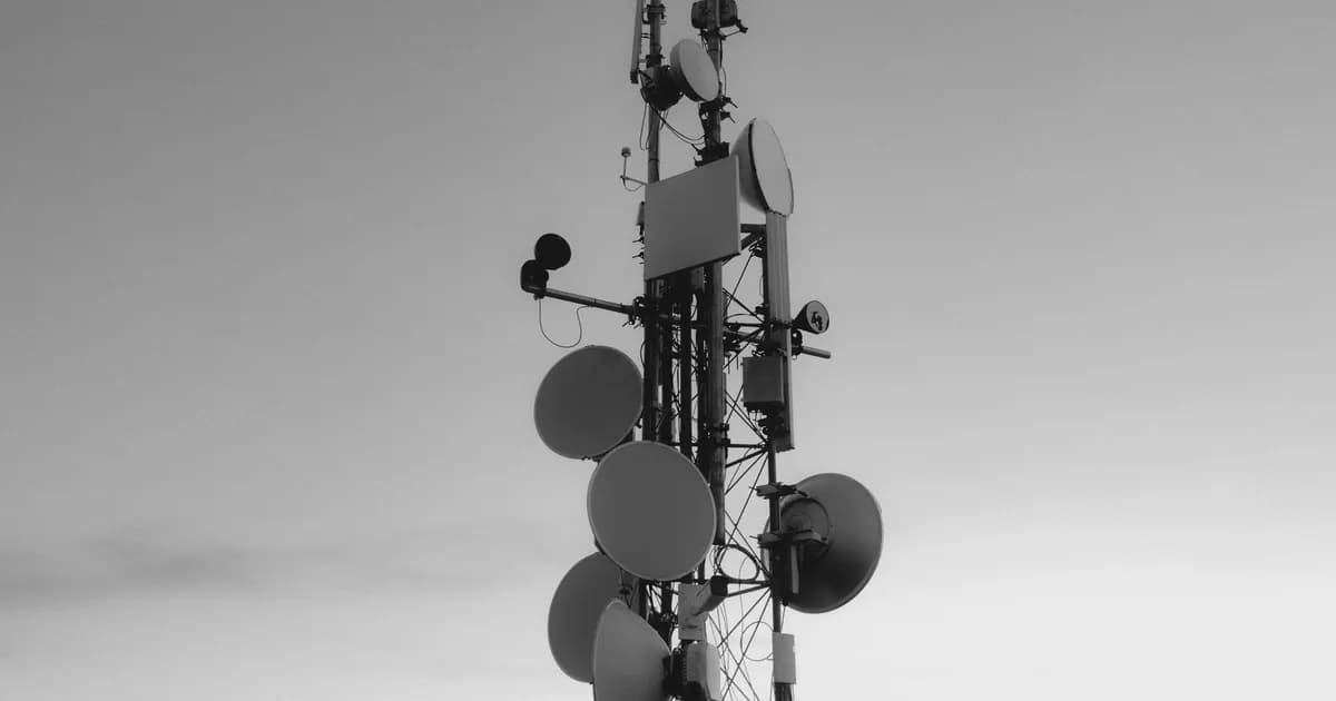 Monochrome image of a tall communications tower with satellite dishes under an expansive sky