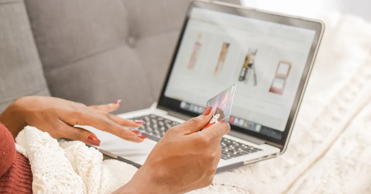 A woman relaxes on a couch while shopping online using her laptop and credit card