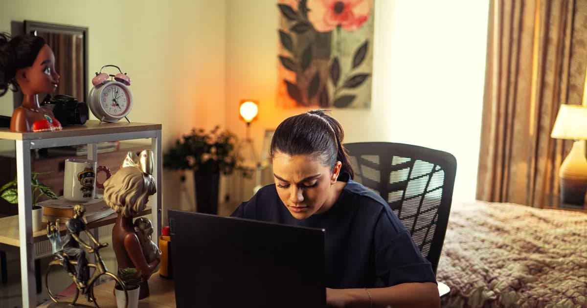 A woman intensely working on a laptop at her home office desk, surrounded by decor