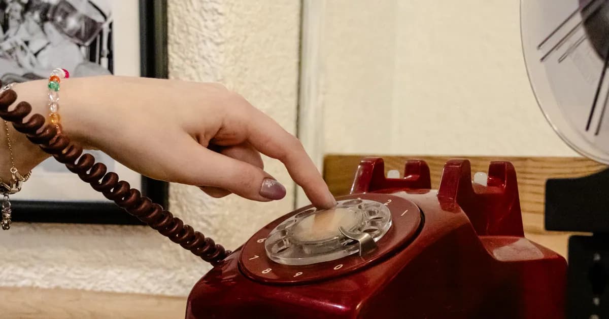 A close-up of a hand dialing a classic red rotary phone
